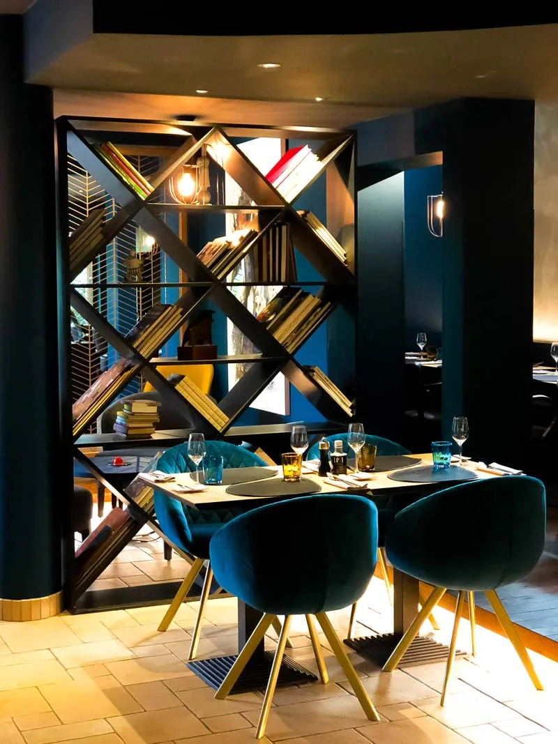 Ronde tafel met blauwe fluwelen stoelen voor een goudkleurig ruitvormig wandrek