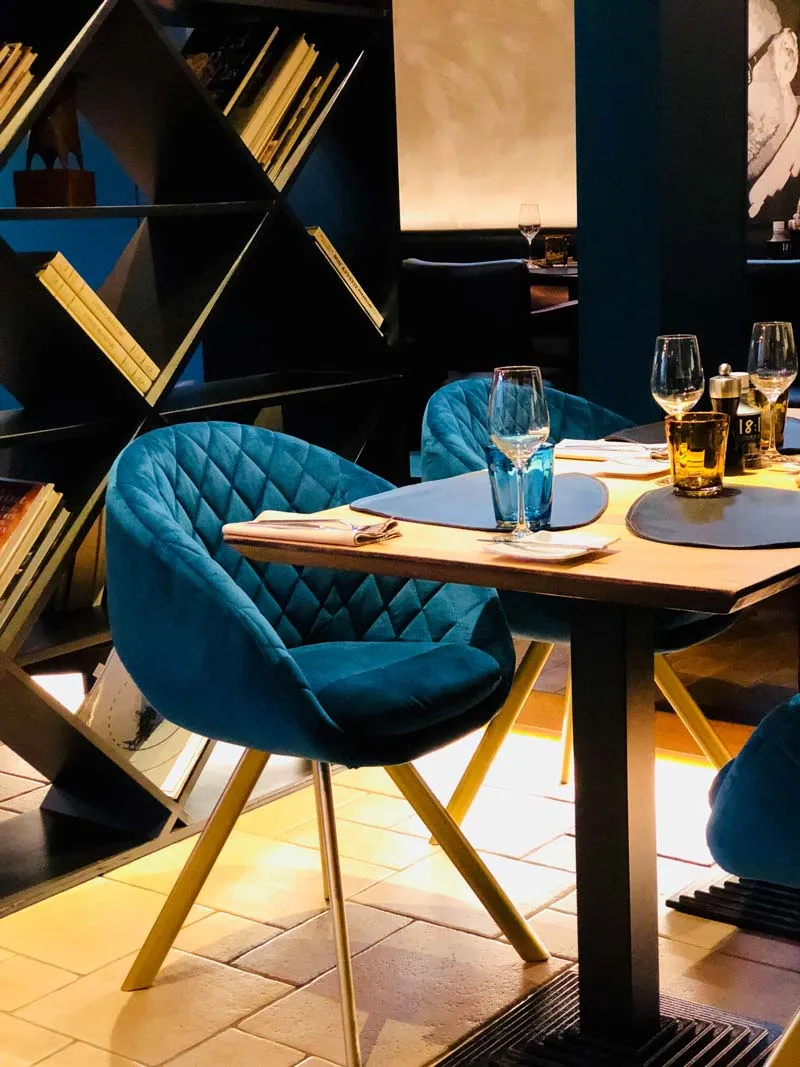 Blauwe fluwelen stoelen aan een gedekte tafel naast het boekenrek